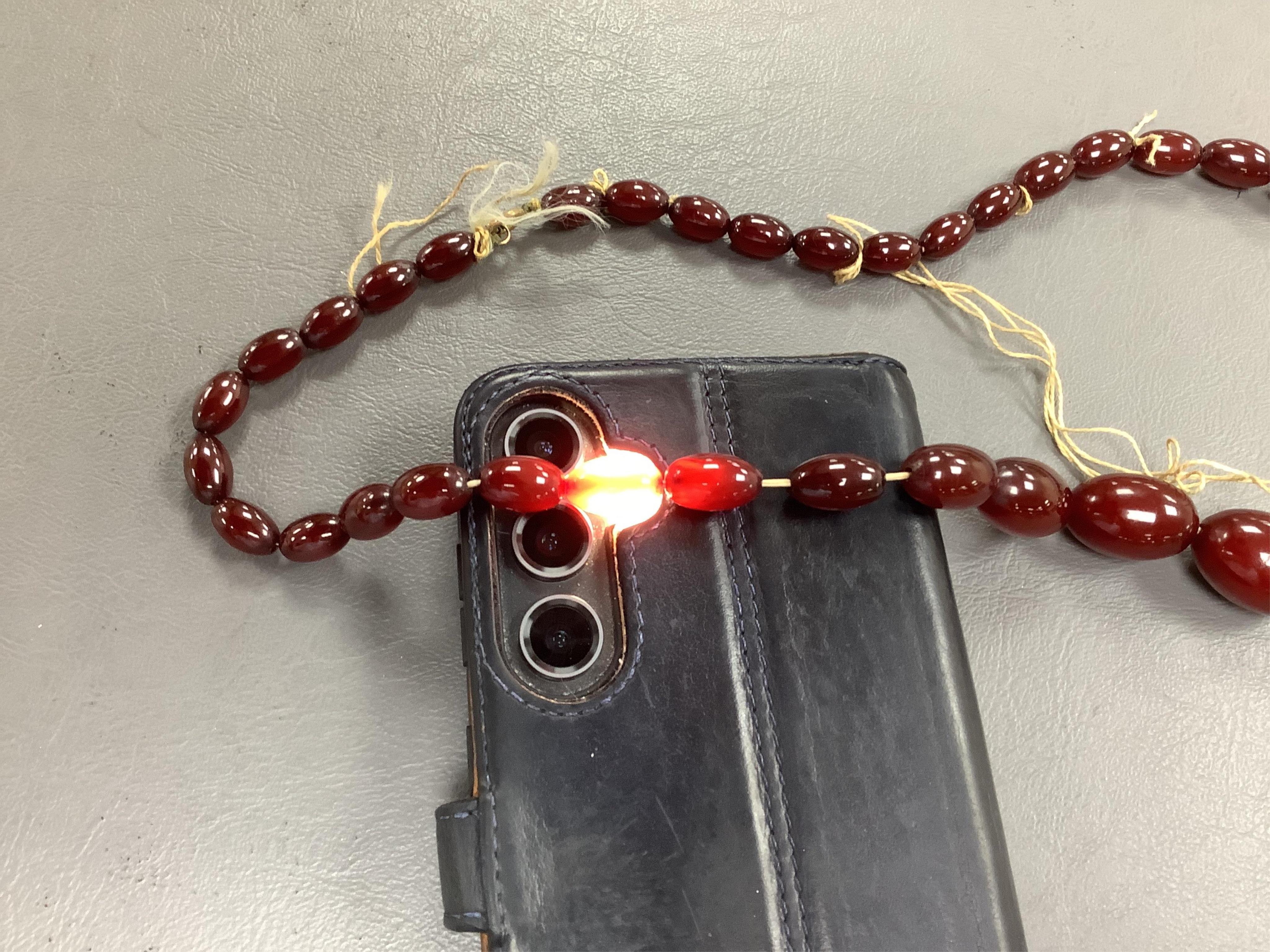 A cherry-coloured bakelite imitation amber necklace, composed of graduated oval beads measuring approximately 1.2-3cm, length 56cm, gross weight approximately 54 grams